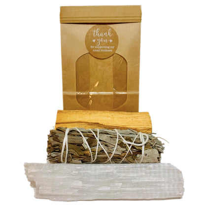 Brown package with a "thank you" sticker, white crystal, sage bundle, and palo santo wood.