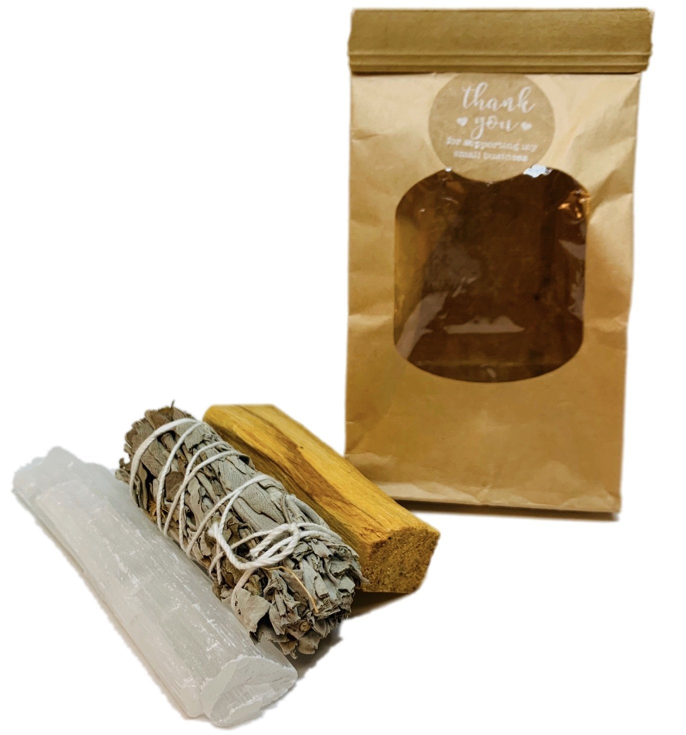 Brown paper bag with palo santo, sage smudge stick, and selenite wand in front.