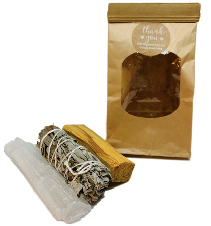 Brown paper bag with palo santo, sage smudge stick, and selenite wand in front.