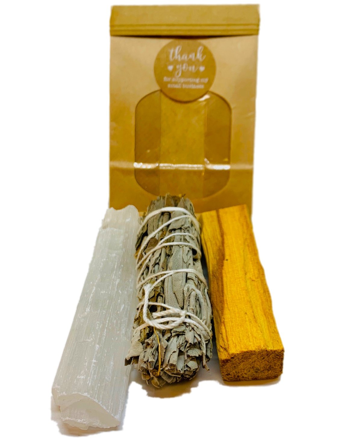 White crystal, bundled sage, and yellow wood stick in front of a brown paper package.