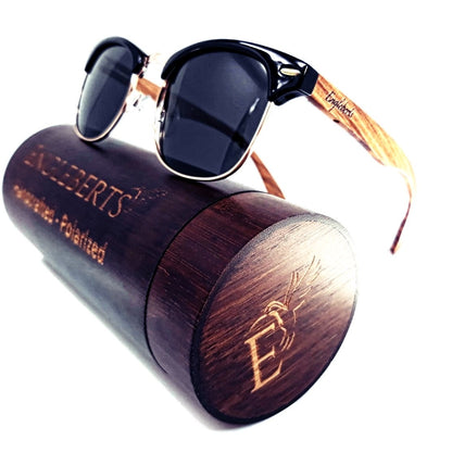 Sunglasses with black frames, wooden arms, on a round wooden case with engraved design.