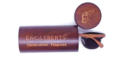 Wooden sunglasses case with engraved text, round lid, and partially visible sunglasses.