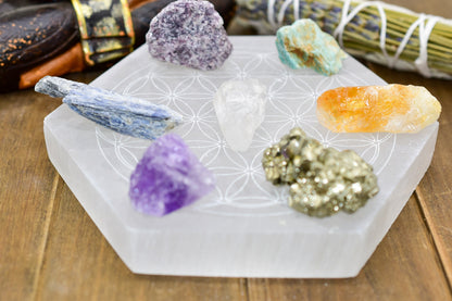 Crystals of various colors on a hexagonal white plate with a floral pattern, atop a wooden surface.