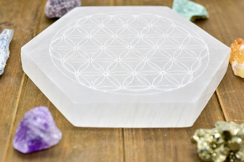 Hexagonal white crystal plate with floral pattern, surrounded by colorful rocks on wooden surface.