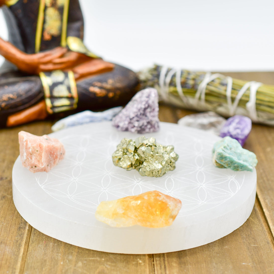 Crystals on a round etched disc with a sage bundle and statue, set on a wooden surface.