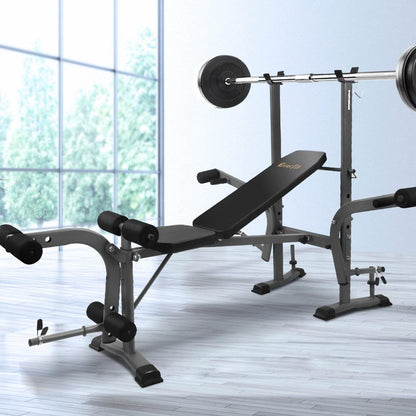 Weight bench with barbell set in a bright room, gray floors, and large windows showing green foliage.