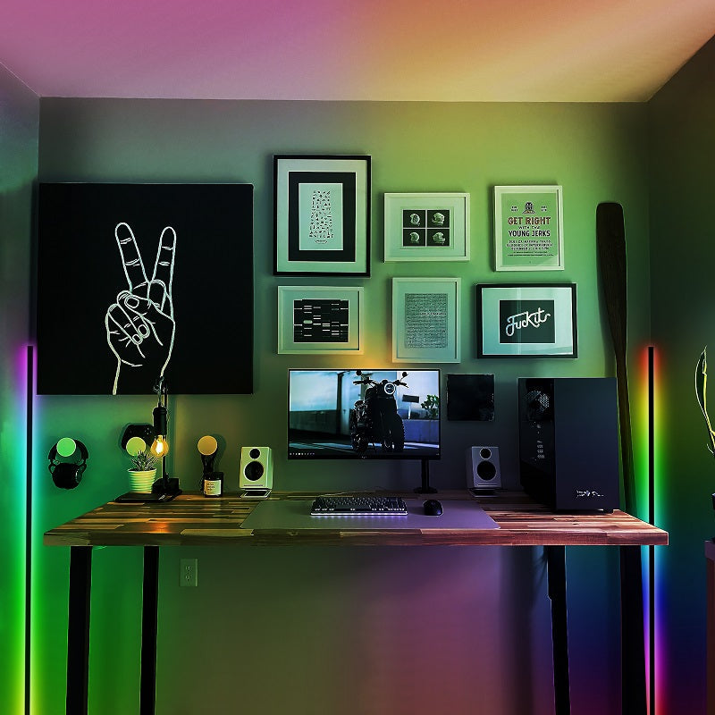 LED-lit desk setup with framed art, a peace sign canvas, and a monitor on a wooden table.