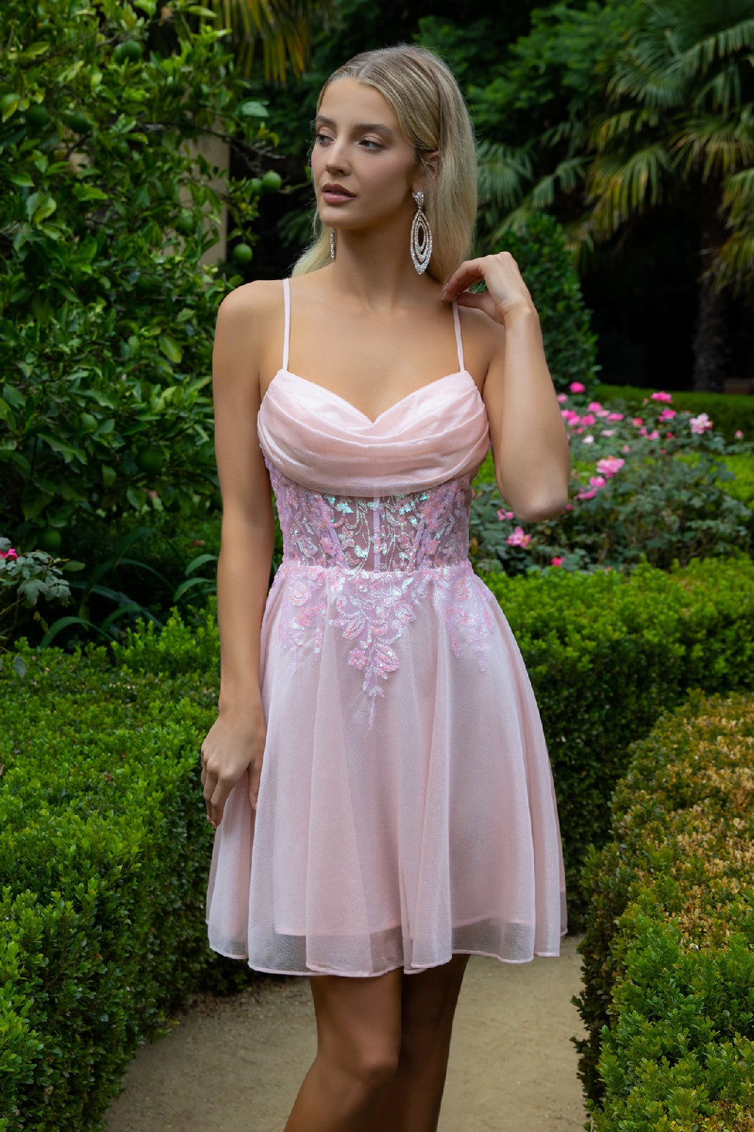 Woman in a pink dress with floral embroidery, standing in a lush garden with pink flowers.