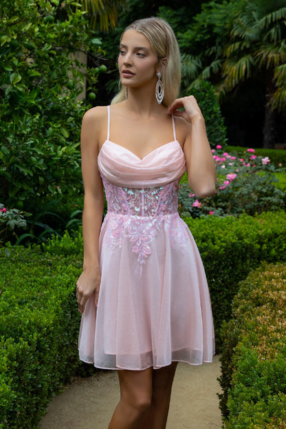 Woman in a pink dress with floral embroidery, standing in a lush garden with pink flowers.