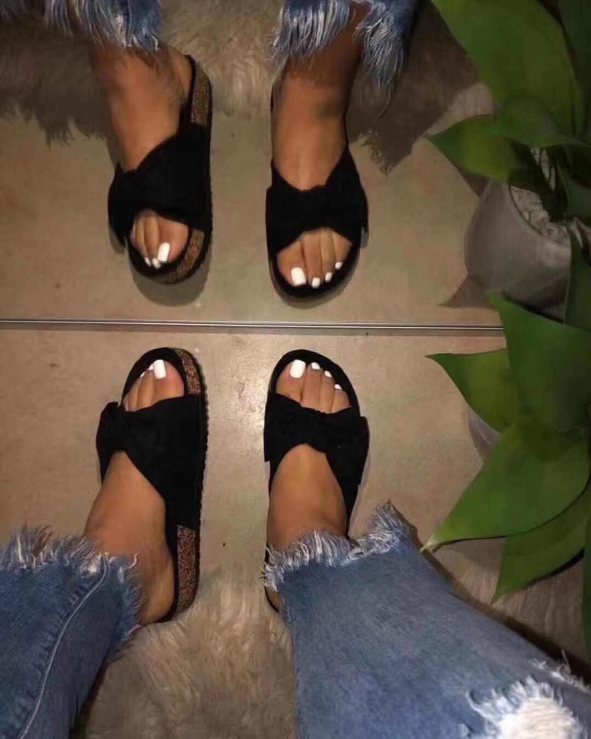 Feet in black bow sandals, white toenails, ripped jeans, mirror reflection, and a green plant.
