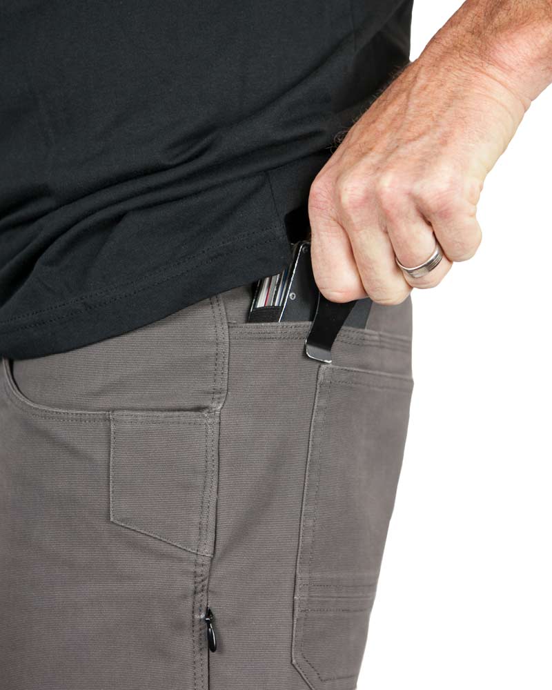Hand placing a black object in gray pants pocket; person wearing a black shirt, with a silver ring.