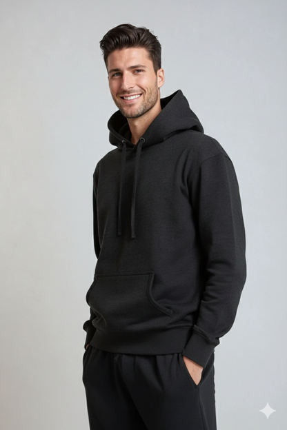 Smiling man in a black hoodie with hands in pockets, set against a light gray background.