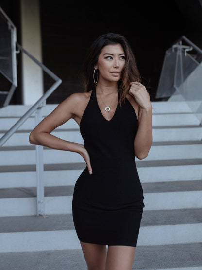 Woman in a black dress with large hoop earrings standing on stairs, hand on hip, looking sideways.