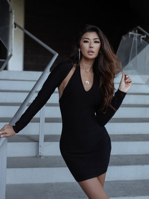 Woman in a black dress on modern stairs, with glass railing and dark background.