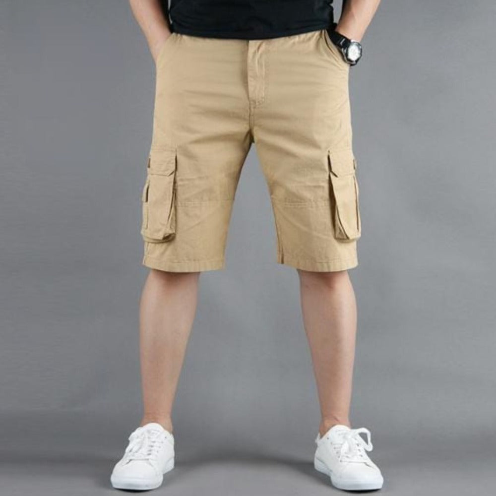 Person wearing beige cargo shorts, white sneakers, and a black shirt against a gray background.