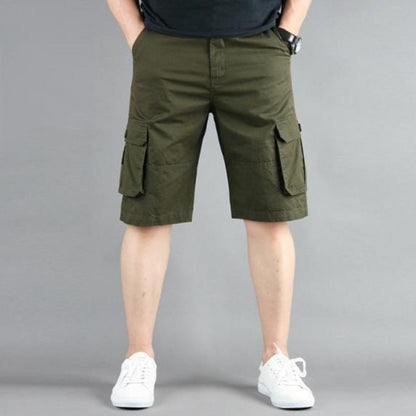 Man in olive cargo shorts and white sneakers against a gray background.