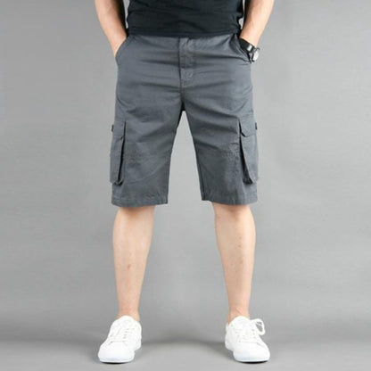 Man in gray cargo shorts and white sneakers against a gray background.