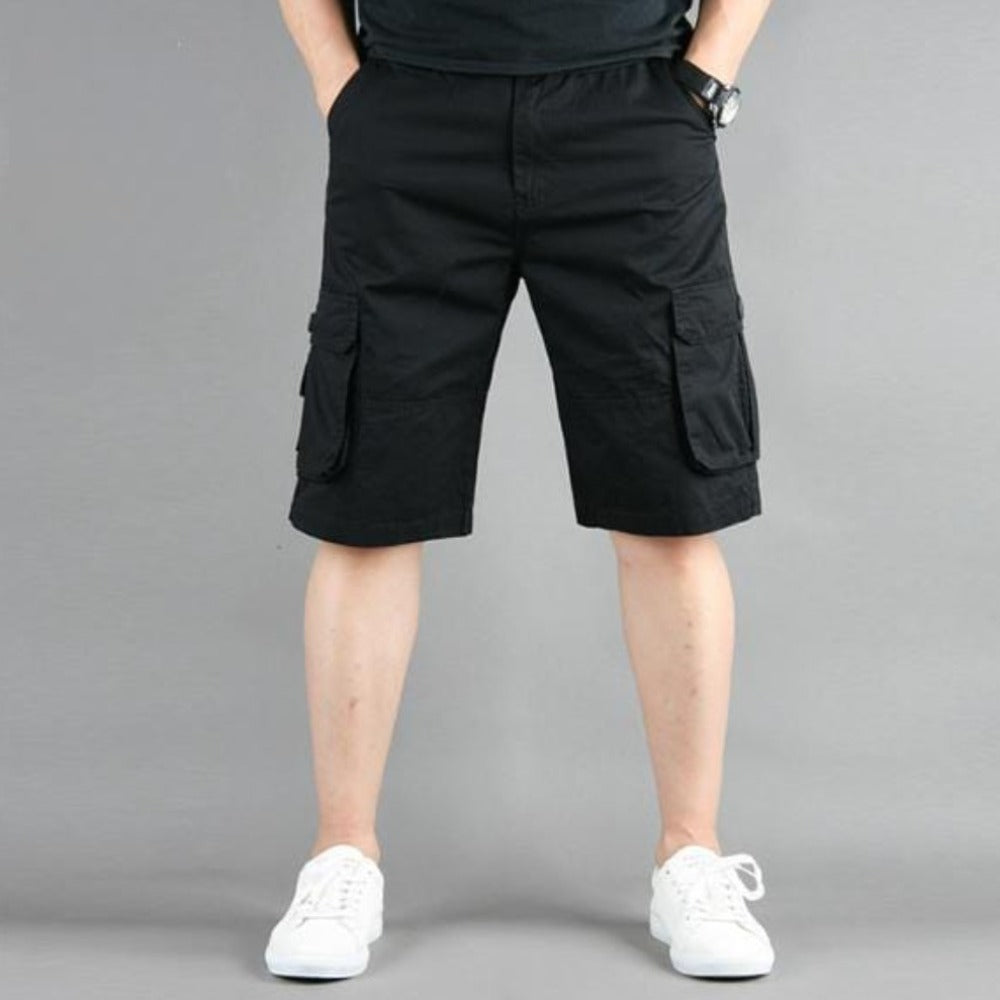 Person wearing black cargo shorts and white sneakers against a gray background.