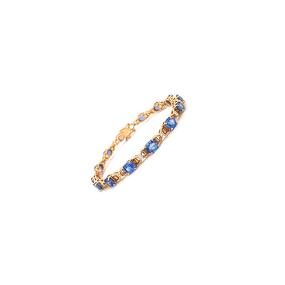 Gold bracelet with blue gemstones in a linked pattern on a white background.