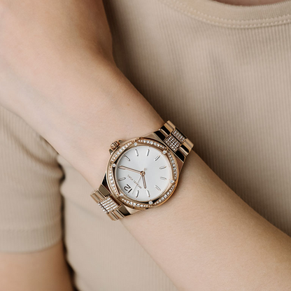 Gold watch with a white face and diamond accents on a wrist, against a beige background.