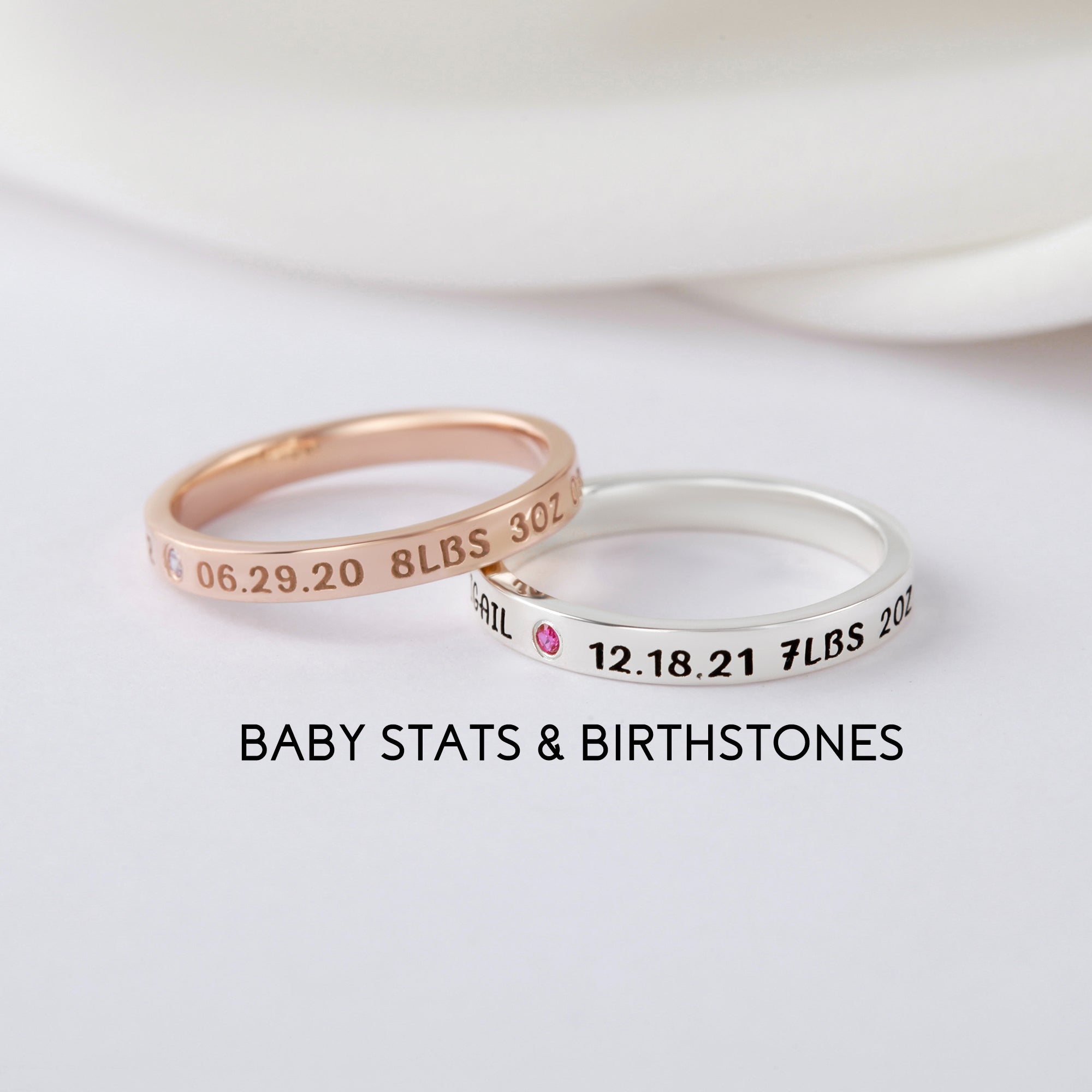 Two engraved rings with birthstones, one rose gold and one silver, on a white surface.