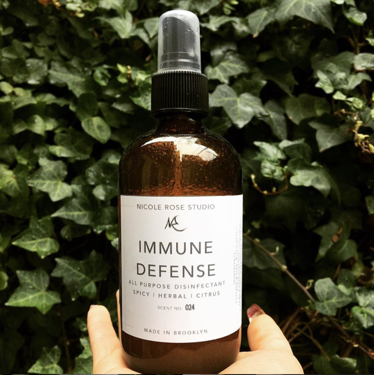 A brown spray bottle labeled "Immune Defense" held against a background of green ivy leaves.