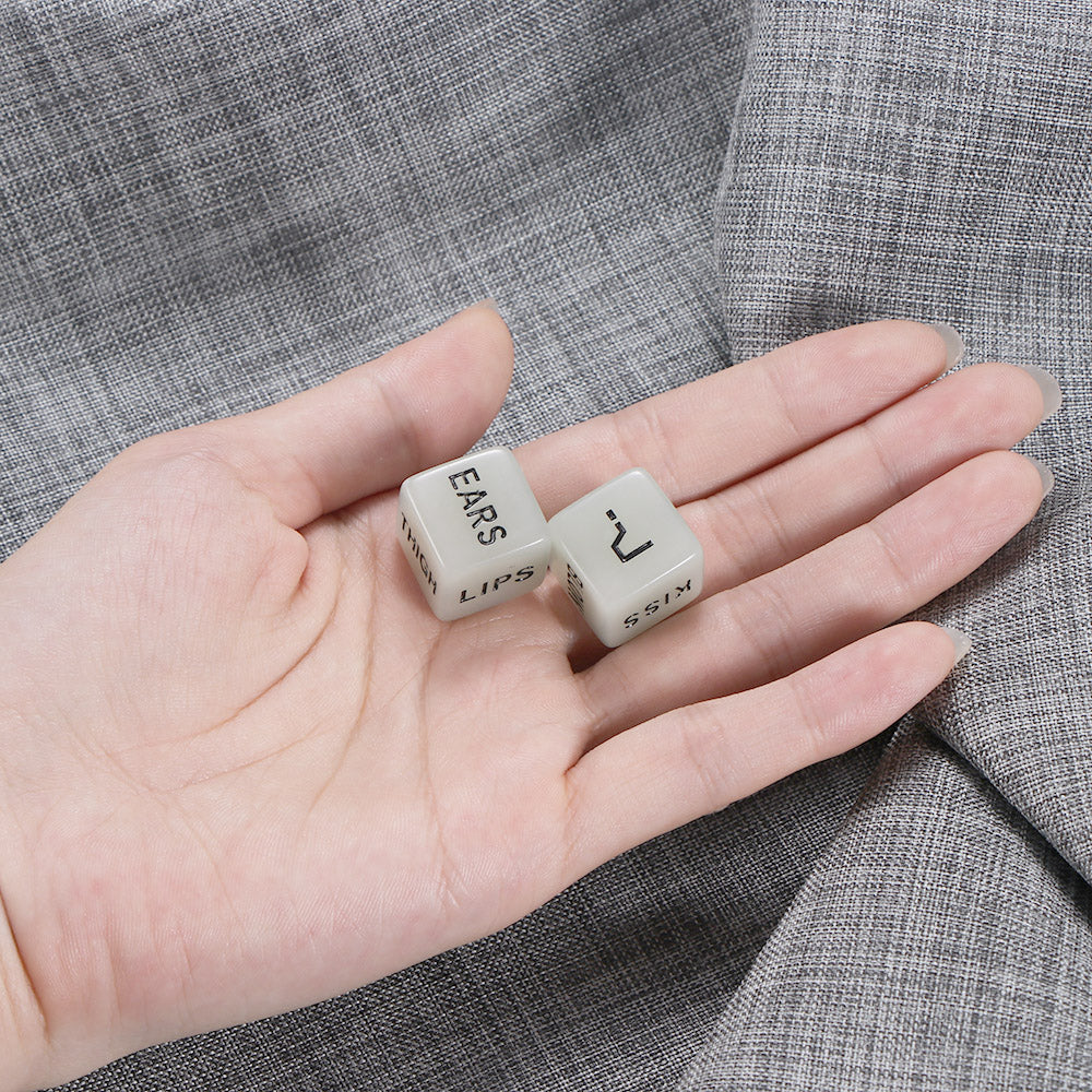 Hand holding two white dice labeled "EARS" and "KISS" on a gray textured fabric background.