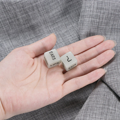 Hand holding two white dice labeled "EARS" and "KISS" on a gray textured fabric background.