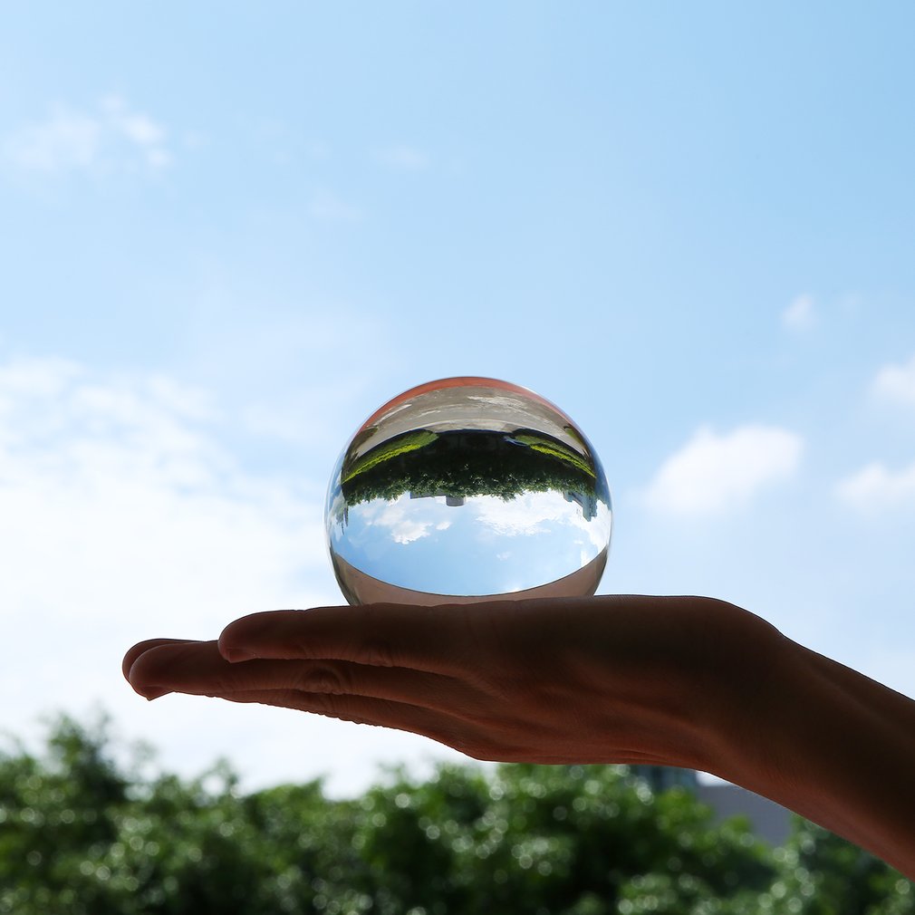 Hand holding a reflective glass sphere, with sky and trees inverted inside it.