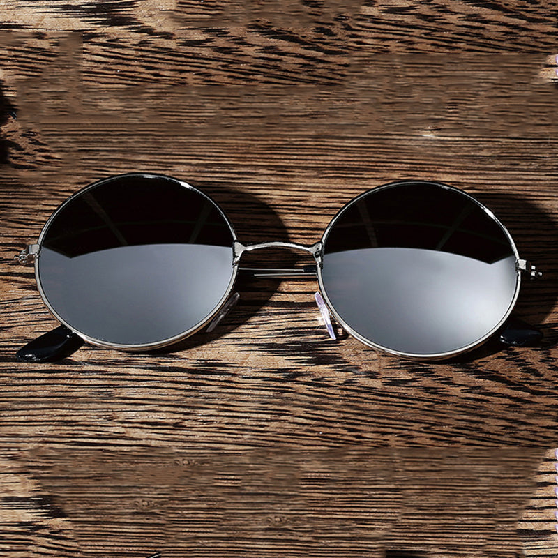Round sunglasses with black lenses and silver frames on a textured wooden surface.