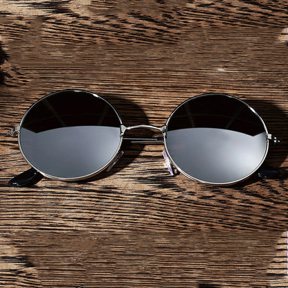 Round sunglasses with black lenses and silver frames on a textured wooden surface.