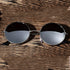 Round sunglasses with black lenses and silver frames on a textured wooden surface.