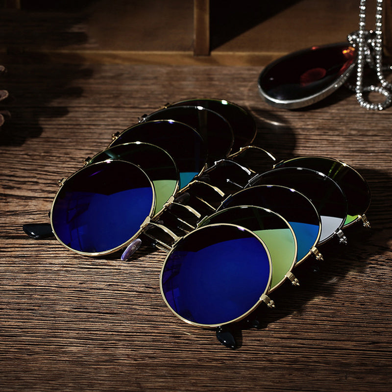 Blue-tinted round sunglasses with gold frames on a wooden surface; chain and a lens nearby.