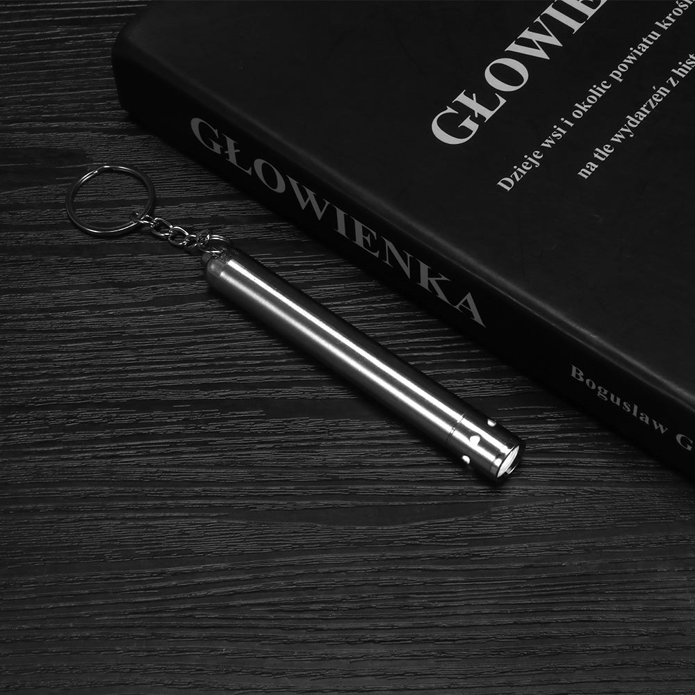 Silver flashlight keychain on dark wood beside a black book with white lettering.