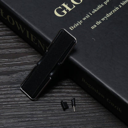 Black device on a textured dark wooden table, near a black book with gold text and small gadgets.