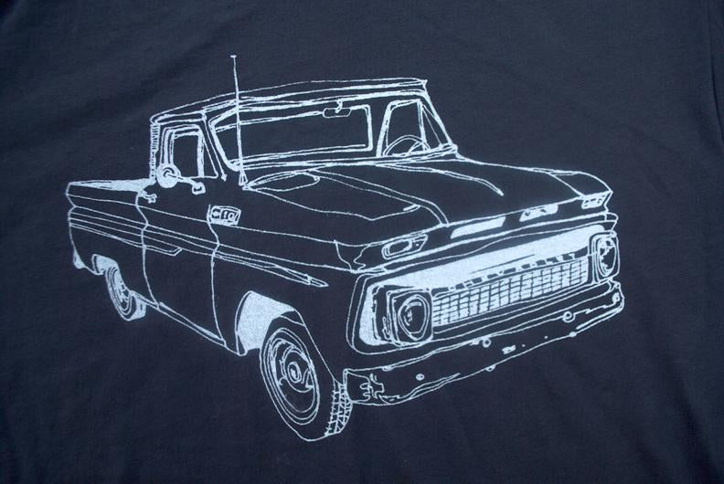 Line drawing of a vintage pickup truck on a dark fabric, outlined in white.