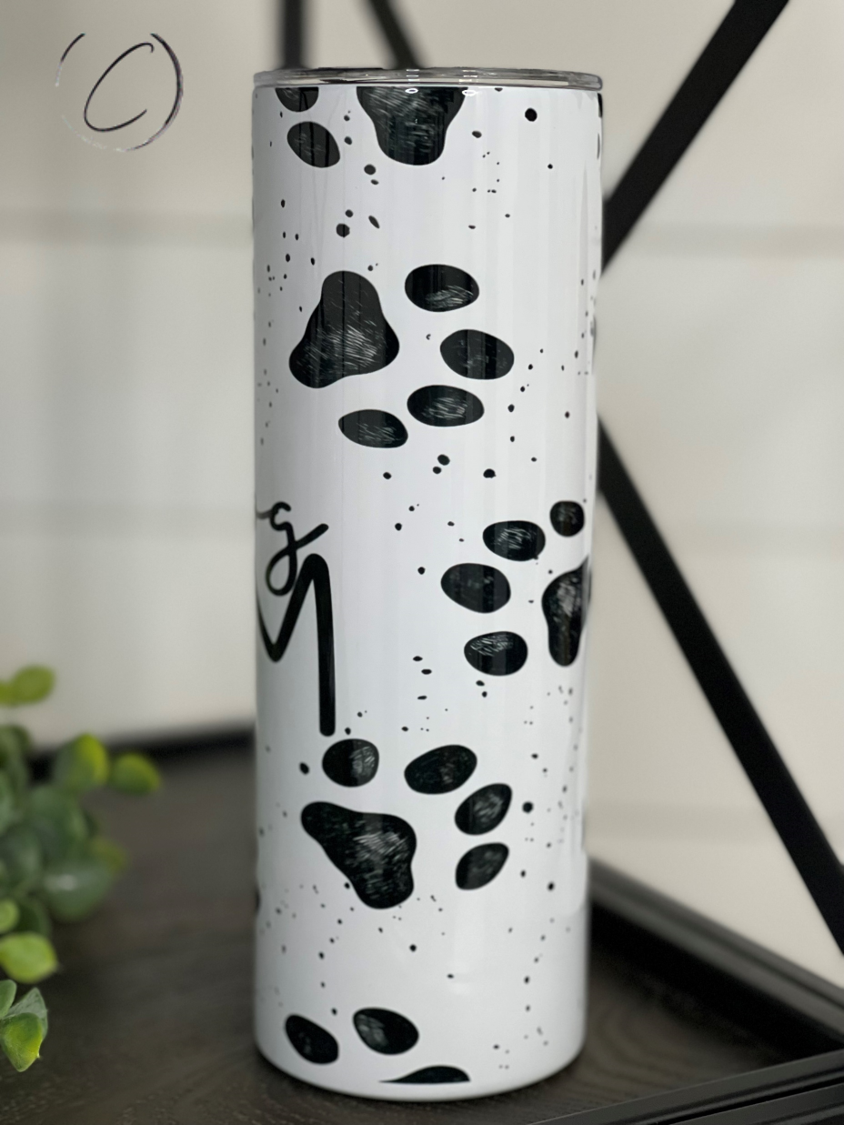 White tumbler with black paw prints, speckles, and a swirl design, on a wooden surface.