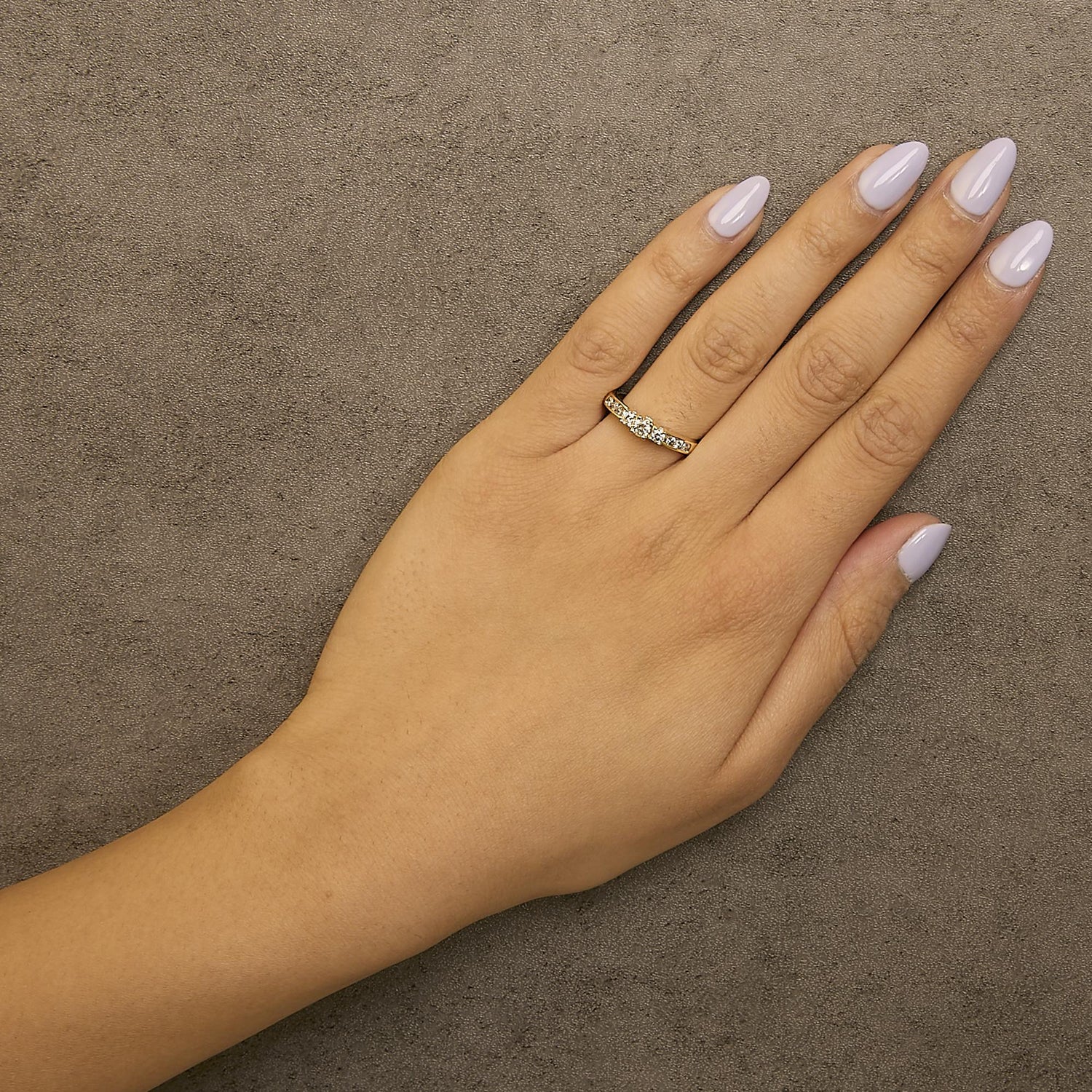 Hand with lavender nails wearing a gold ring with diamonds on a textured gray background.