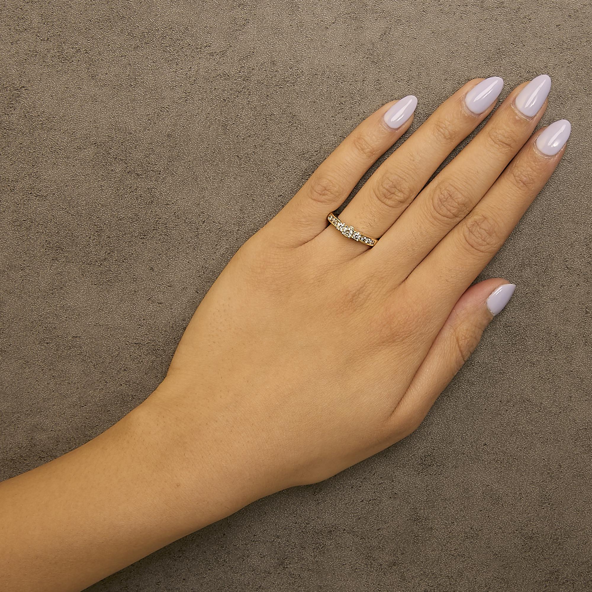 Hand with lavender nails wearing a gold ring with diamonds on a textured gray background.
