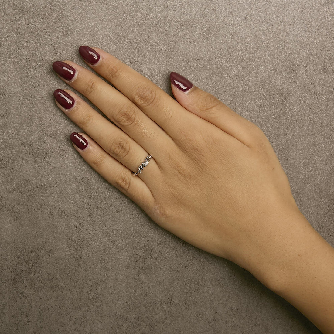 Hand with maroon nails and a silver ring against a textured gray background.