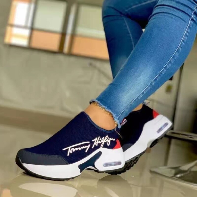 Blue slip-on sneaker with white logo, white sole, red accents; worn with blue jeans.