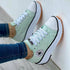 Mint green sneakers with white toe caps, black trims, and orange ridged soles on a wooden floor.