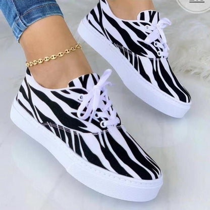 Zebra-patterned sneakers with white soles and laces, worn with a gold anklet.