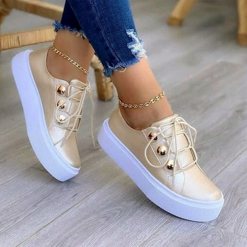 Gold sneakers with thick white soles and gold eyelets, worn with ripped blue jeans and anklets.