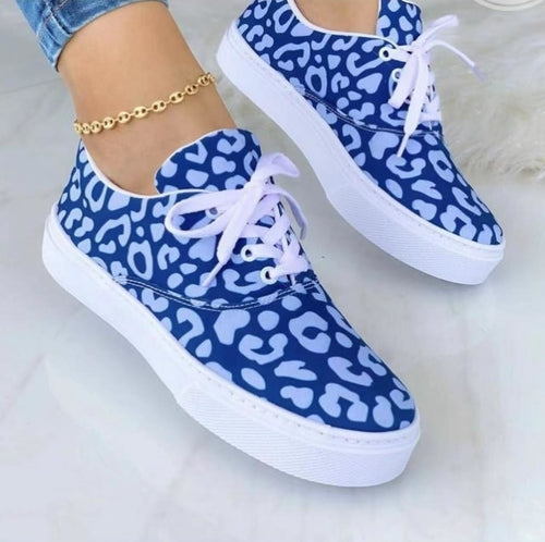 Blue sneakers with white animal print, white soles, and laces on a marble floor, anklet visible.