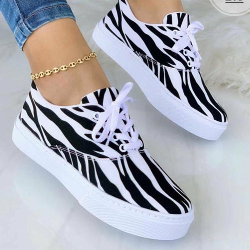 Person wearing zebra-striped sneakers with white soles and laces, paired with a gold anklet.