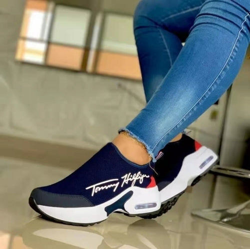 Person wearing blue jeans and navy slip-on sneakers with a white sole and red accents.