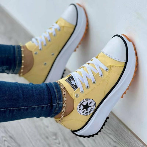 Yellow sneakers with white soles and laces, worn with blue jeans and a gold anklet.