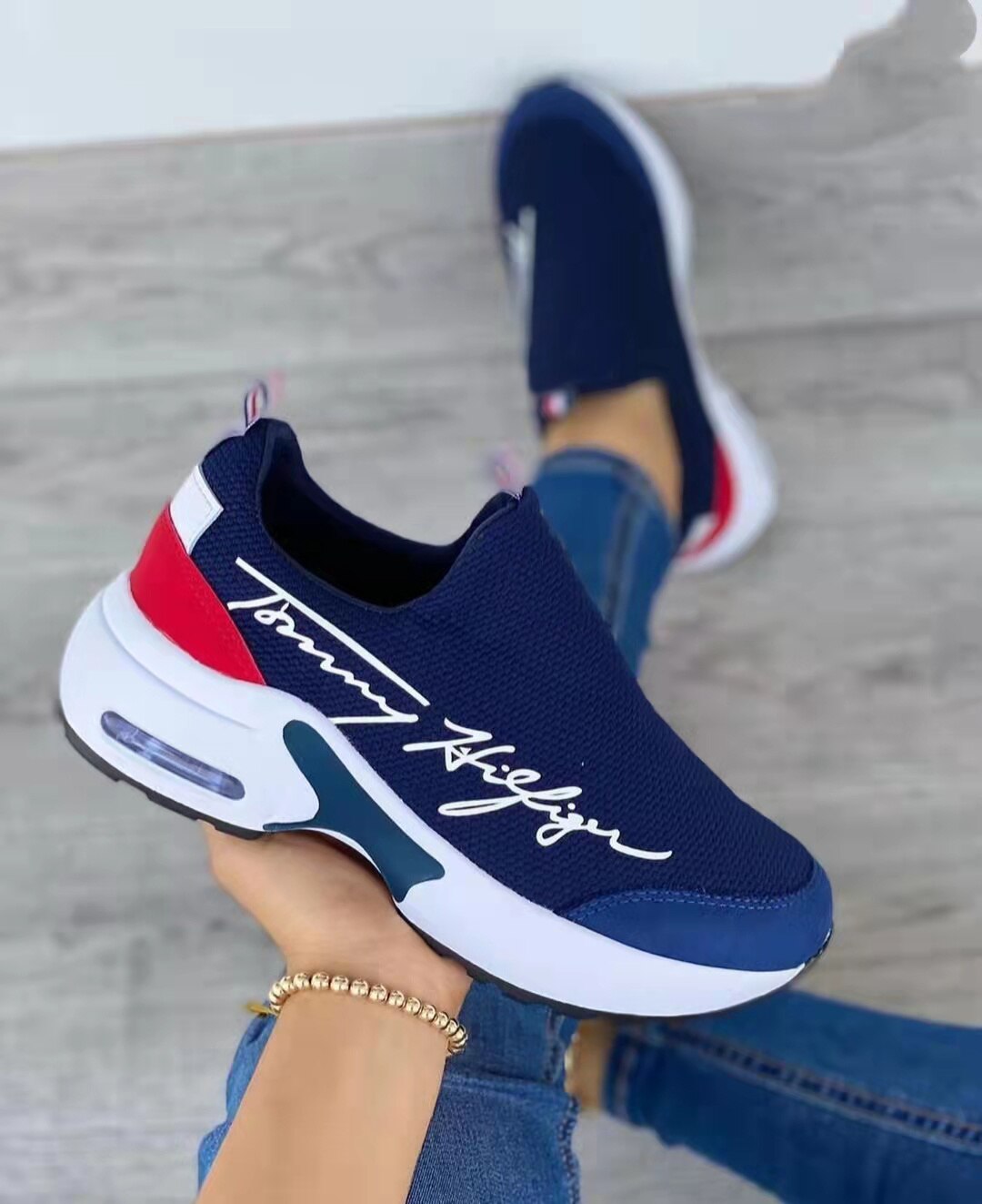Navy blue slip-on sneakers with white sole and red accents, featuring cursive text on the side.