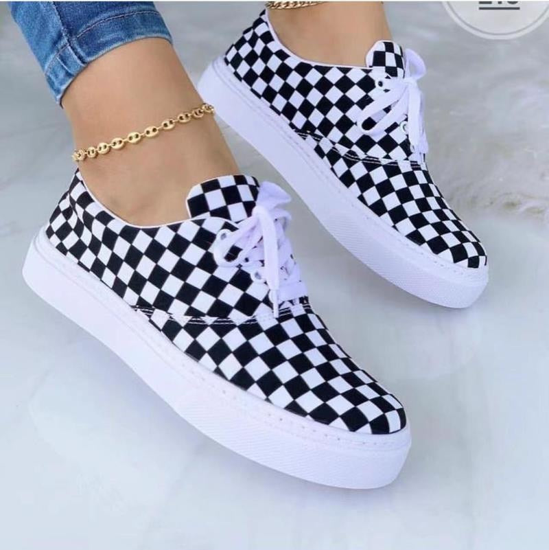 Checkerboard sneakers with white laces and gold anklet on an ankle, worn with blue jeans.